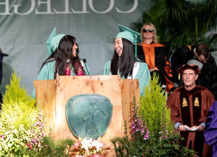 两个学生站在毕业典礼的讲台上，面带微笑